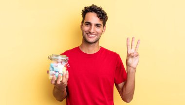 İspanyol yakışıklı adam gülümsüyor ve arkadaş canlısı görünüyor, üç numarayı gösteriyor. şeker konsepti