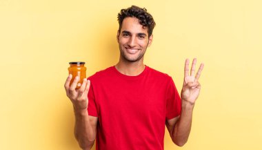 İspanyol yakışıklı adam gülümsüyor ve arkadaş canlısı görünüyor, üç numarayı gösteriyor. Şeftali reçeli