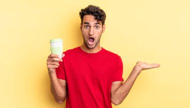 İspanyol yakışıklı adam şaşırmış ve şok olmuş görünüyor. Çenesi düşmüş ve elinde bir nesne var. kahve konseptini kaldır.