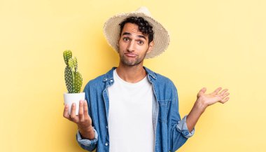 Hispanik yakışıklı adam şaşkın, şaşkın ve şüpheci çiftçi ve kaktüs kavramı