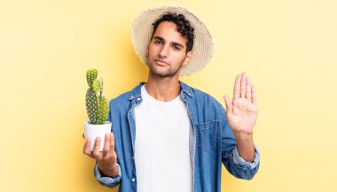 İspanyol yakışıklı adam ciddi görünüyor. Avuç içi gösteriyor. Jest yapan çiftçi ve kaktüs kavramını durduruyor.