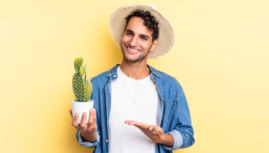 İspanyol yakışıklı adam neşeyle gülümsüyor, mutlu hissediyor ve bir konsept çiftçi ve kaktüs kavramı gösteriyor.