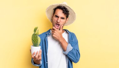 Ağzı ve gözleri açık, elleri çene çiftçisi ve kaktüs kavramının üzerinde olan İspanyol asıllı yakışıklı bir adam.