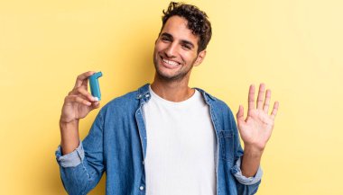 İspanyol yakışıklı adam mutlu bir şekilde gülümsüyor, el sallıyor, seni selamlıyor ve selamlıyor. astım konsepti