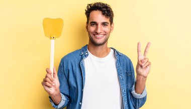 İspanyol yakışıklı adam gülümsüyor ve arkadaş canlısı görünüyor, iki numarayı gösteriyor. Sinekleri öldürür