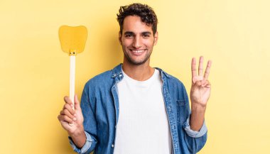 İspanyol yakışıklı adam gülümsüyor ve arkadaş canlısı görünüyor, üç numarayı gösteriyor. Sinekleri öldürür