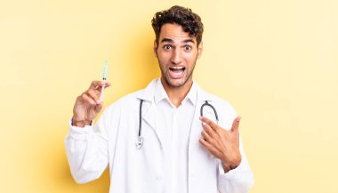 İspanyol yakışıklı adam mutlu hissediyor ve heyecanlı bir doktor ve srynge konseptiyle kendini işaret ediyor.