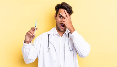 İspanyol görünümlü yakışıklı adam şok olmuş, korkmuş veya korkmuş, yüzünü el hekimi ve srynge konseptiyle kaplamış.