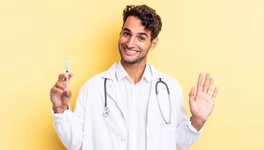 İspanyol yakışıklı adam mutlu bir şekilde gülümsüyor, el sallıyor, sizi selamlıyor ve selamlıyor doktor ve srynge konsepti