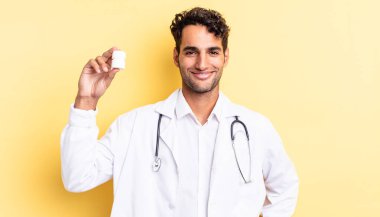 İspanyol yakışıklı adam mutlu bir şekilde gülümsüyor, eli kalçasında ve kendinden emin. Hekim şişesi hapları konsepti