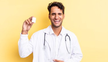 İspanyol yakışıklı bir adam komik bir şakaya yüksek sesle gülüyor. Hekim şişesi hapları konsepti