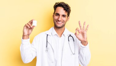 İspanyol yakışıklı adam kendini mutlu hissediyor, iyi bir jestle onaylıyor. Hekim şişesi hapları konsepti