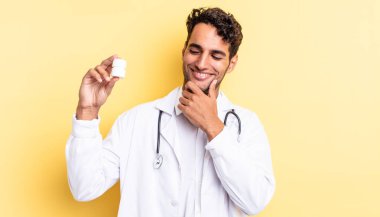 Mutlu, kendine güvenen, elleri çenesinde gülümseyen İspanyol yakışıklı bir adam. Hekim şişesi hapları konsepti