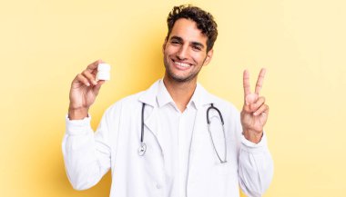 İspanyol yakışıklı adam gülümsüyor ve mutlu görünüyor, zafer ya da barış işareti yapıyor. Hekim şişesi hapları konsepti