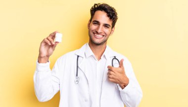 İspanyol yakışıklı adam kendini gururlu hissediyor, başparmağıyla olumlu gülümsüyor. Hekim şişesi hapları konsepti