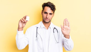 İspanyol yakışıklı adam ciddi görünüyor. Avuç içi gösteriyor. Durdurma hareketi yapıyor. Hekim şişesi hapları konsepti