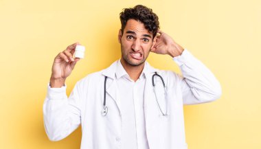 İspanyol yakışıklı adam kendini stresli, endişeli ya da korkmuş hissediyor, elleri başının üstünde. Hekim şişesi hapları konsepti