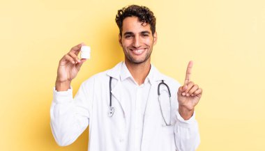 İspanyol yakışıklı adam gülümsüyor ve arkadaş canlısı görünüyor, bir numarayı gösteriyor. Hekim şişesi hapları konsepti