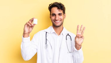 İspanyol yakışıklı adam gülümsüyor ve arkadaş canlısı görünüyor, üç numarayı gösteriyor. Hekim şişesi hapları konsepti