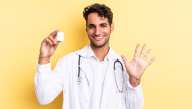 İspanyol yakışıklı adam gülümsüyor ve arkadaş canlısı görünüyor, beş numarayı gösteriyor. Hekim şişesi hapları konsepti