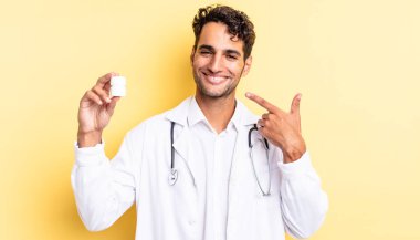 İspanyol yakışıklı adam kendine güvenerek gülüyor ve kendi gülüşüne işaret ediyor. Hekim şişesi hapları konsepti