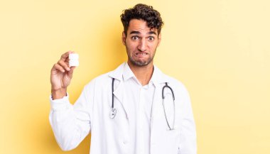 İspanyol yakışıklı adam kafası karışmış ve şaşkın görünüyor. Hekim şişesi hapları konsepti