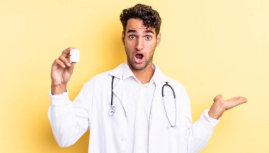 İspanyol yakışıklı adam şaşırmış ve şok olmuş görünüyor. Çenesi düşmüş ve elinde bir nesne var. Hekim şişesi hapları konsepti