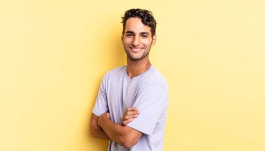 İspanyol yakışıklı adam kameraya kollarını kavuşturup gülümsüyor.