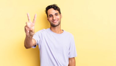 İspanyol yakışıklı adam gülümsüyor ve mutlu görünüyor, zafer ya da barış işareti yapıyor.
