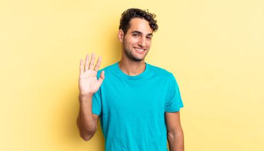 İspanyol yakışıklı adam mutlu bir şekilde gülümsüyor, el sallıyor, seni selamlıyor ve selamlıyor.