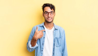 İspanyol yakışıklı adam mutlu, gururlu ve şaşırmış görünüyor, neşeyle kendini işaret ediyor.