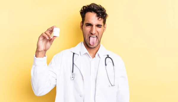 陽気で反抗的な態度を持つパニックハンサムな男冗談と舌を突き出す 医師用ボトル薬のコンセプト — ストック写真