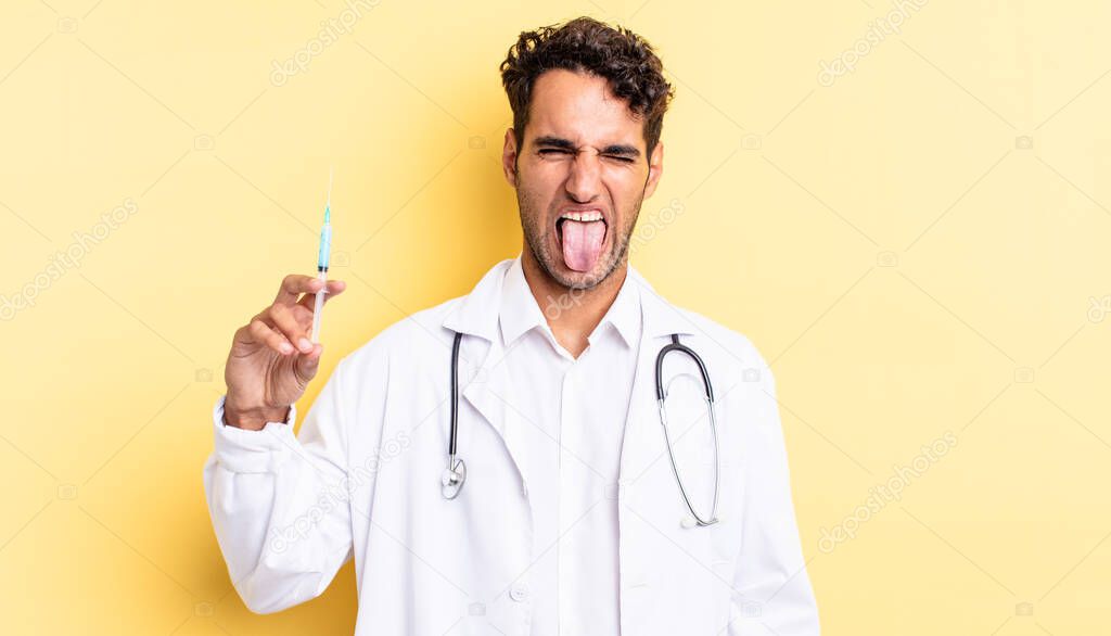 hispanic handsome man with cheerful and rebellious attitude, joking and sticking tongue out physician and srynge concept