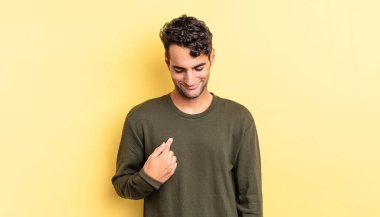 İspanyol yakışıklı adam gülümsüyor, aşağıya bakıyor ve göğsünü işaret ediyor.