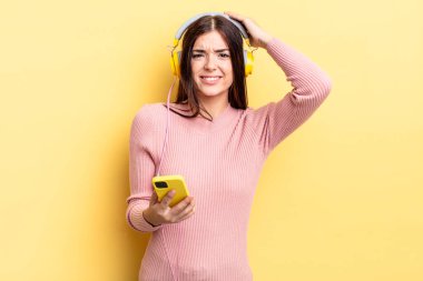 Genç İspanyol kadın stresli, endişeli ya da korkmuş hissediyor, elleri başının üstünde. kulaklıklar ve telefon konsepti