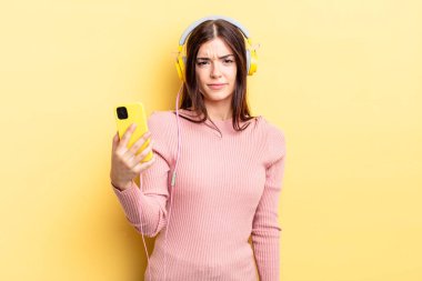 Genç İspanyol kadın üzgün, üzgün ya da kızgın hissediyor ve yana bakıyor. kulaklıklar ve telefon konsepti