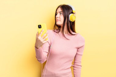 Profil görünümlü genç İspanyol kadın hayal mi kuruyor yoksa hayal mi kuruyor? kulaklıklar ve telefon konsepti