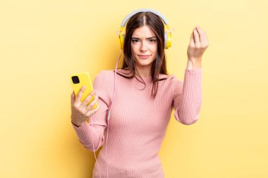 Genç İspanyol kadın kapiş ya da para hareketi yapıyor, sana ödemeni söylüyor. kulaklıklar ve telefon konsepti