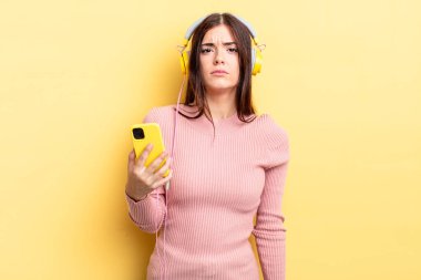 Genç İspanyol kadın üzgün ve mızmızlanıyor. Mutsuz bir bakışı var ve ağlıyor. kulaklıklar ve telefon konsepti