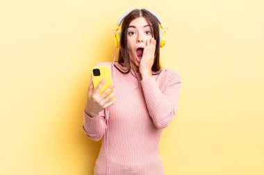 Genç İspanyol kadın şok olmuş ve korkmuş hissediyor. kulaklıklar ve telefon konsepti