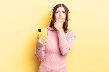 Genç İspanyol kadın düşünüyor, kuşkulu ve şaşkın hissediyor. kulaklıklar ve telefon konsepti