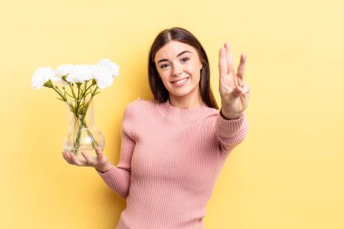 Genç İspanyol kadın gülümsüyor ve arkadaş canlısı görünüyor, üç numarayı gösteriyor. saksı konsepti