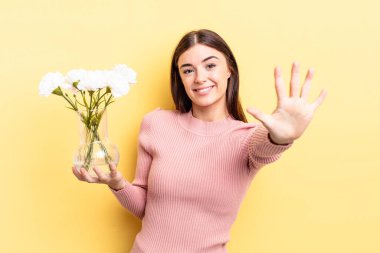 Genç İspanyol kadın gülümsüyor ve arkadaş canlısı görünüyor, beş numarayı gösteriyor. saksı konsepti