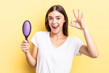 Genç İspanyol kadın kendini mutlu hissediyor, iyi bir jestle onaylıyor. saç fırçası konsepti