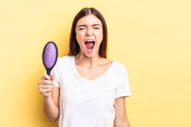 Genç İspanyol kadın agresif bir şekilde bağırıyor, çok kızgın görünüyor. saç fırçası konsepti