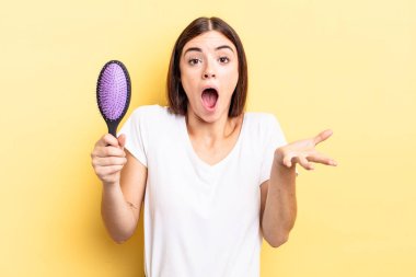 Genç İspanyol kadın şok olmuş ve şaşırmış hissediyor. saç fırçası konsepti