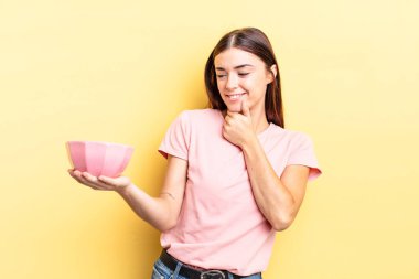 Genç İspanyol kadın mutlu ve kendinden emin bir ifadeyle gülümsüyor. Elleri çenesinde. boş kase kavramı