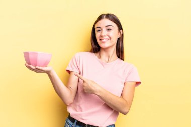 Genç İspanyol kadın neşeyle gülümsüyor, mutlu hissediyor ve bir tarafı işaret ediyor. boş kase kavramı