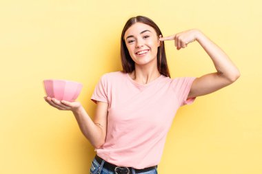 Genç İspanyol kadın kendine güvenerek gülümsüyor ve kendi gülüşünü gösteriyor. boş kase kavramı