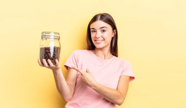 Genç İspanyol kadın neşeyle gülümsüyor, mutlu hissediyor ve bir tarafı işaret ediyor. kahve çekirdeği konsepti